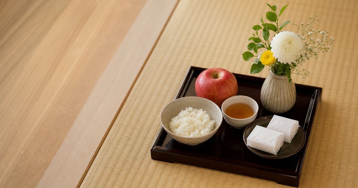 仏壇に供えるご飯、お茶、和菓子、果物、花が一枚の盆にまとめて並べられている写真