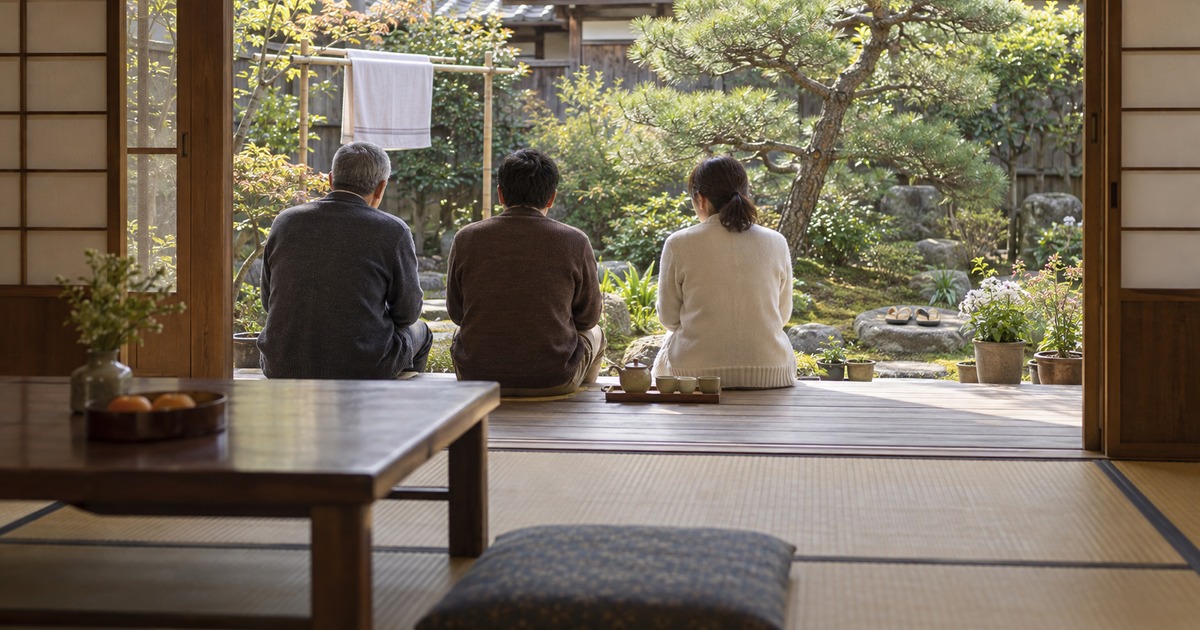 実家の縁側に大人のきょうだい3人が並んで腰掛け、庭を眺めながら話している後ろ姿の写真